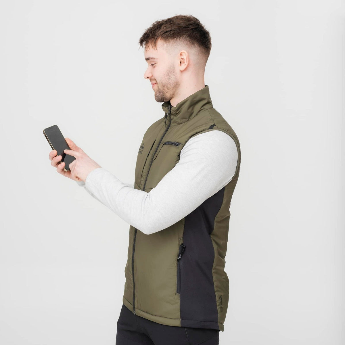 En man i olivgrön HeatX Hunt Vest styr värmen i mobilen