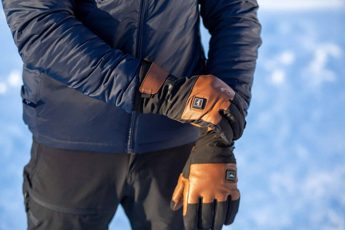 En man drar åt manschetten på ett par skinnhandskar med värme i snön