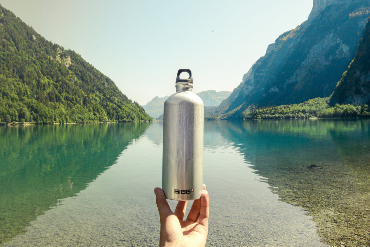 En SIGG Traveller i aluminium hålls upp framför en fjällsjö