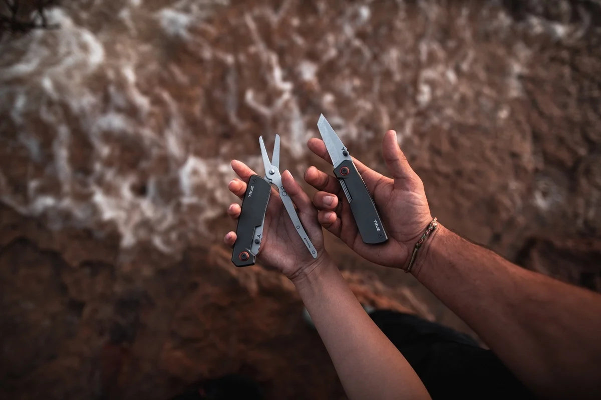 Två händer håller upp True Dual Cutter med utfällt knivblad och sax